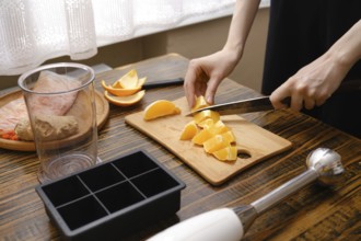 A person is cutting fresh oranges on a wooden board in a kitchen. The sunlight is coming through
