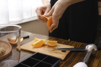 A person peels orange slices on a wooden cutting board in the kitchen during the process of