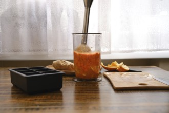 Mixing sea buckthorn and orange in a jar with immersion blender on a wooden table near the window .