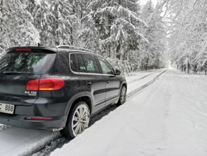 SUV driving in lane across heavily snow-covered road with lots of snow through a winter forest,