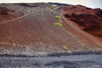Red volcanic landscape with sparse vegetation and people at the top of a hill, El Golfo Lanzarote