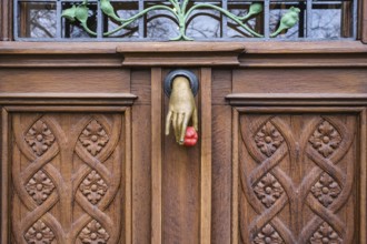 A cast iron door knocker on a wooden, artfully decorated front door in the shape of a hand holding