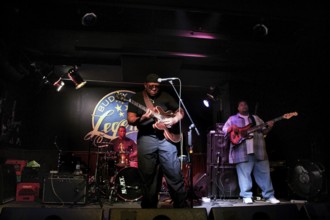 Blues musicians perform vividly on a club stage, accompanied by intensive guitar and drum music,
