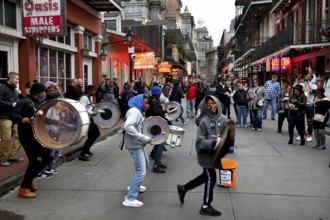 Musicians play on bustling Bourbon Street in the French Quarter. Drums and people create a lively