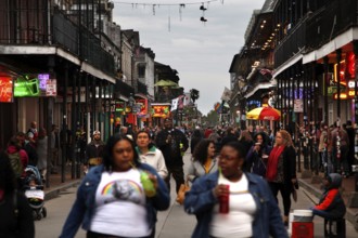 Lively nighttime scene on Bourbon Street with numerous passers-by and illuminated shops, New