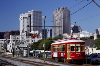 Red streetcar in front of city skyline with skyscrapers on a sunny day, New Orleans, Louisiana, USA