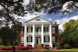 Large mansion with white pillars and well-kept garden, framed by mature trees, Natchez,