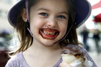 Happy girl with chocolate ice cream on her face smiles at the camera. Wears a summer hat, Savannah,