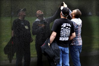 Men look at and touch the engravings of the wall of the Vietnam Veterans Memorial in a thoughtful