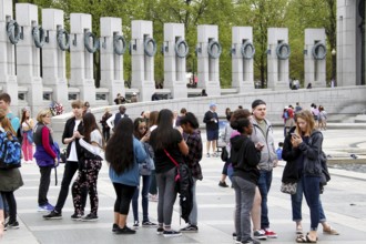 People group together at a memorial with tall pillars. The atmosphere is calm and respectful,