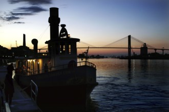 Silhouette of a ship on the Savannah River at sunset. A bridge can be seen in the background,