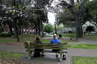 Two people sitting on a bench in Chippewa Square enjoying the park, Savannah, Georgia, USA