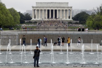 Visitors in front of a fountain looking at a historic monument in the distance, Washington D.C, USA