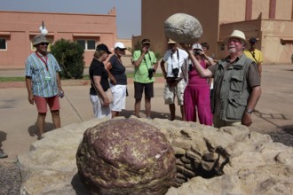 Group of tourists taking a guided tour of the CLA Studios in front of a big rock, Ouarzazate,