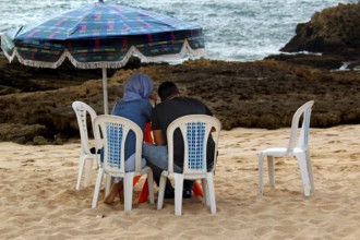Two people sitting under a colorful sunshade on the beach in Oulidia, Oulidia, Morocco