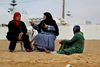 Three woman in traditional dress talking on the beach in Oulidia, Oulidia, Morocco