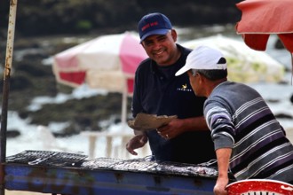 Two men talking at a food stall on the shore with a view of the sea, Oulidia, Doukkala-Abda,