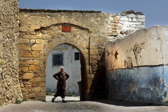 A man stands under an old stone arch in the medina of Safi, Safi, Doukkala-Abda, Morocco