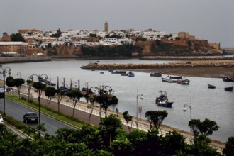 View across the river to the historic town of Salé with boats and city wall under cloudy sky,
