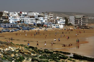 Busy beach with fishing boats and white buildings on the shore, Taghazout, Souss-Massa region,