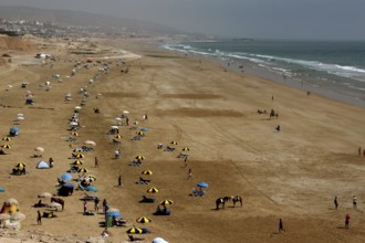Busy sandy beach of Taghazout with lots of umbrellas and people at the sea, Taghazout, Souss-Massa