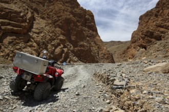 A quad bike rides through a rocky gorge under a clear sky, Tal, Tizgui n'Ouadda