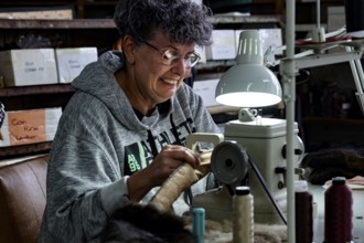 Seamstress works concentrated with thread and material under a lamp in a Possum factory, Stratford,