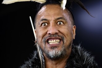 Maori man with remarkable facial expression and feather decoration during performance, Rotorua, Bay