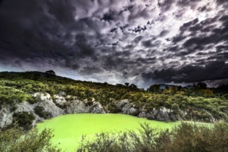 Geothermal area with bright green lagoon under dramatic cloudy skies, Wai-O-Tapu, New Zealand