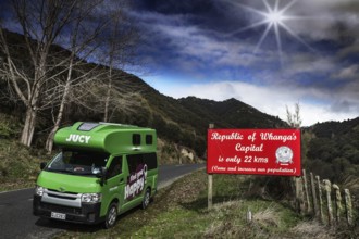 Campervan stands next to a Whangamomona Republic sign in a rural, sunny landscape, Whangamomona,