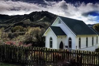 White church against wooded mountains under dramatic sky in Whangamomona, Whangamomona, New Zealand