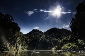 The sun shines over the wooded hills of the Whanganui River and meets calm water, zero