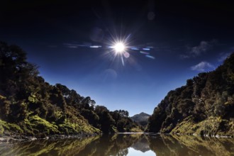 Sunlight falls on peaceful landscape of the Whanganui River with wooded hills and calm water, zero