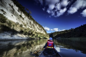 Paddler on calm river between high cliffs under bright blue sky near Whanganui River, zero