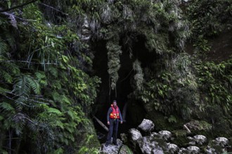 A person in a cave in the green, moss-covered forest near the Whanganui River on a canoe trip, zero