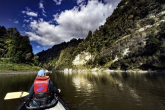 Person in a canoe paddles along steep, wooded cliffs under a dramatic sky, zero