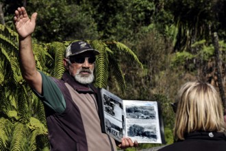 Tour guide points to surroundings surrounded by nature and holds a book, Whanganui River, New