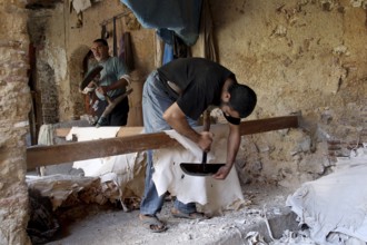 A man works on leather goods in an old workshop with rustic charm, Fez, Fez el Bali, Morocco