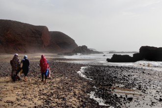 Tourists wearing colorful jackets walking on Legzira beach, Legzira, Souss-Massa region, Morocco