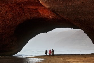 Impressive rock arch spanning the beach with silhouettes of visitors, Legzira, Souss-Massa region,