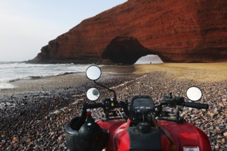 Quad bike on beach with impressive rock arch in Legzira, Legzira, Morocco