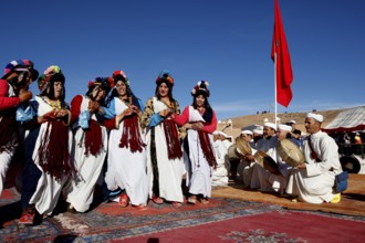Women perform traditional Berber dance with an ensemble of musicians in the background under a blue