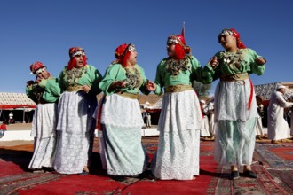 Dancing woman in traditional Berber clothes on colorful carpet during the Fête des Roses, El Kelâa