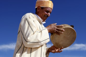 Smiling man playing drum during Fête des Roses in front of a clear sky, El Kelâa m'Gouna,