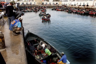 Boats in the calm waters of the harbor with fishermen working on the quay wall, El Jadida, harbor,
