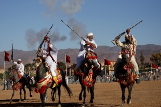 Three horsemen pass each other with rifles in traditional clothing, surrounded by dusty landscape,