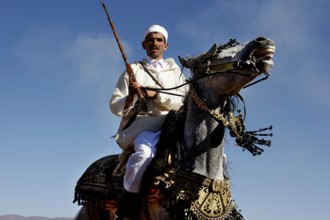 A man in traditional traditional costume rides a magnificently decorated horse under a blue sky, El