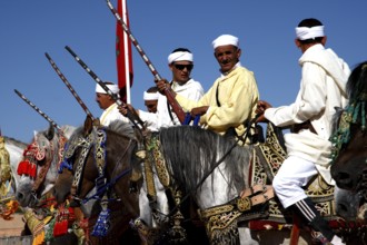 Horsemen in a group under blue skies perform a Fantasia performance, El Kelâa m'Gouna, Morocco