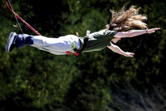 Female jumper in full length across the countryside bungee jumping, Queenstown, Otago, New Zealand