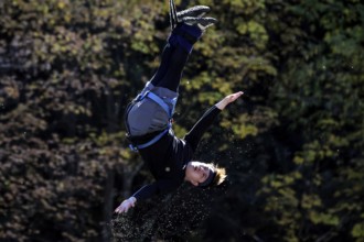 Single jumper doing a somersault in the air in front of an autumn tree backdrop, Queenstown, Otago,